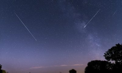 A star-filled purplish night sky, with two meteors streaking across
