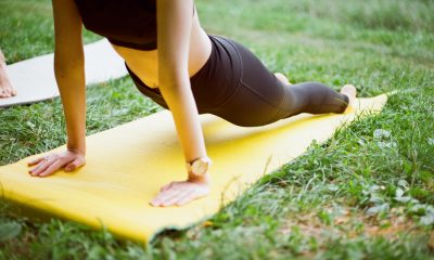 Female person doing a yoga stretch on a yellow mat outdoors, on top of grass